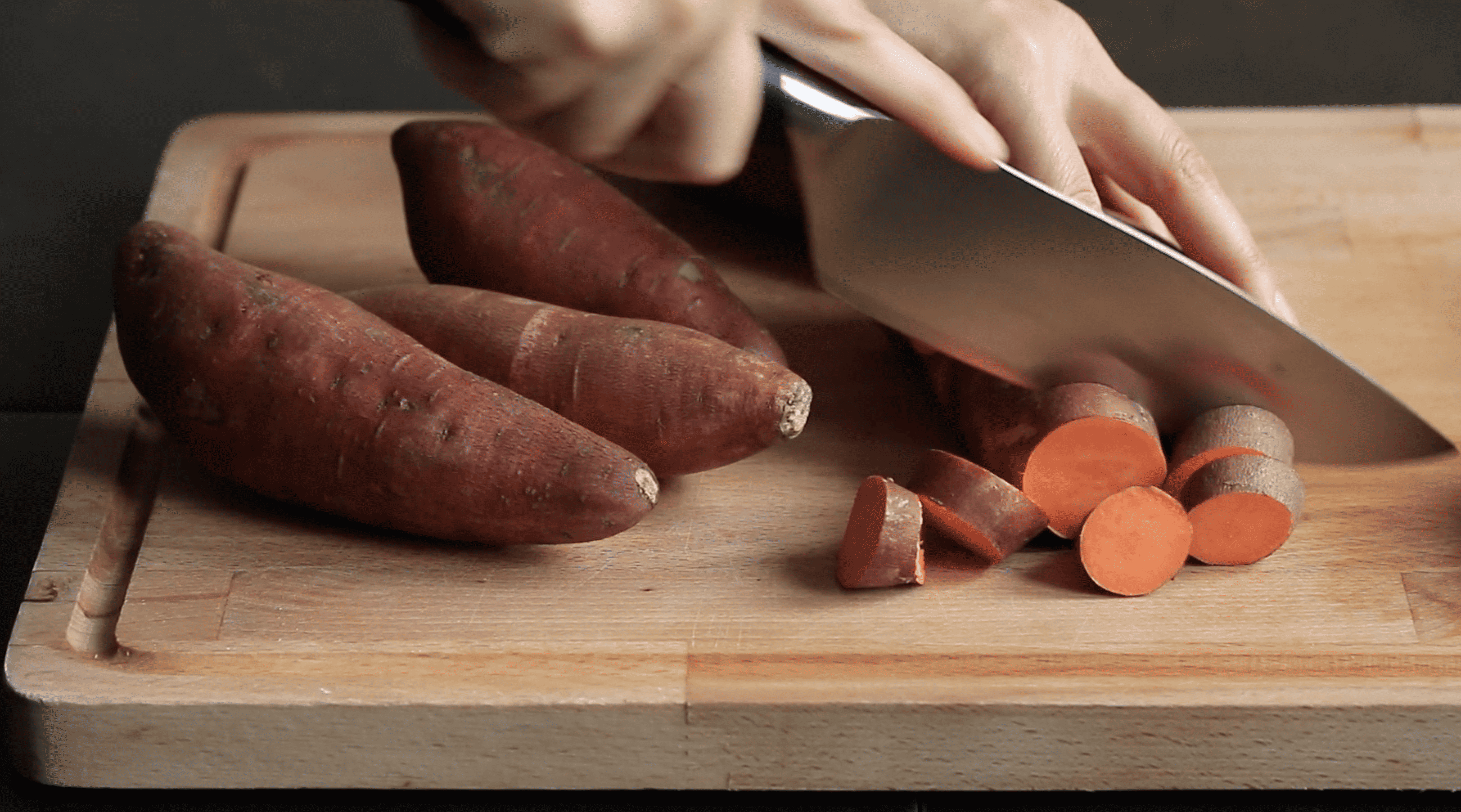 hands chopping sweet potatoes on a cutting board