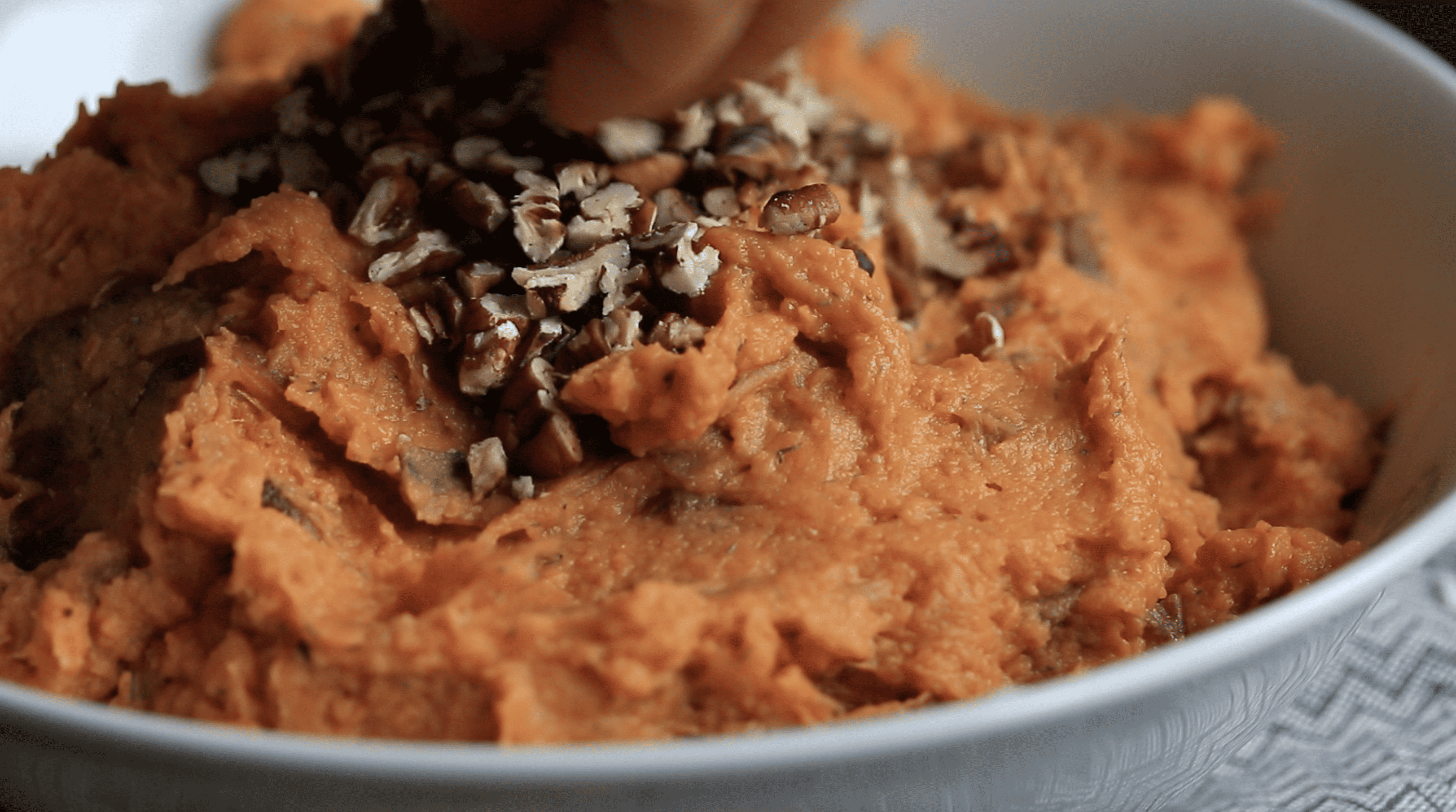 hand adding chopped pecans to sweet potato mash