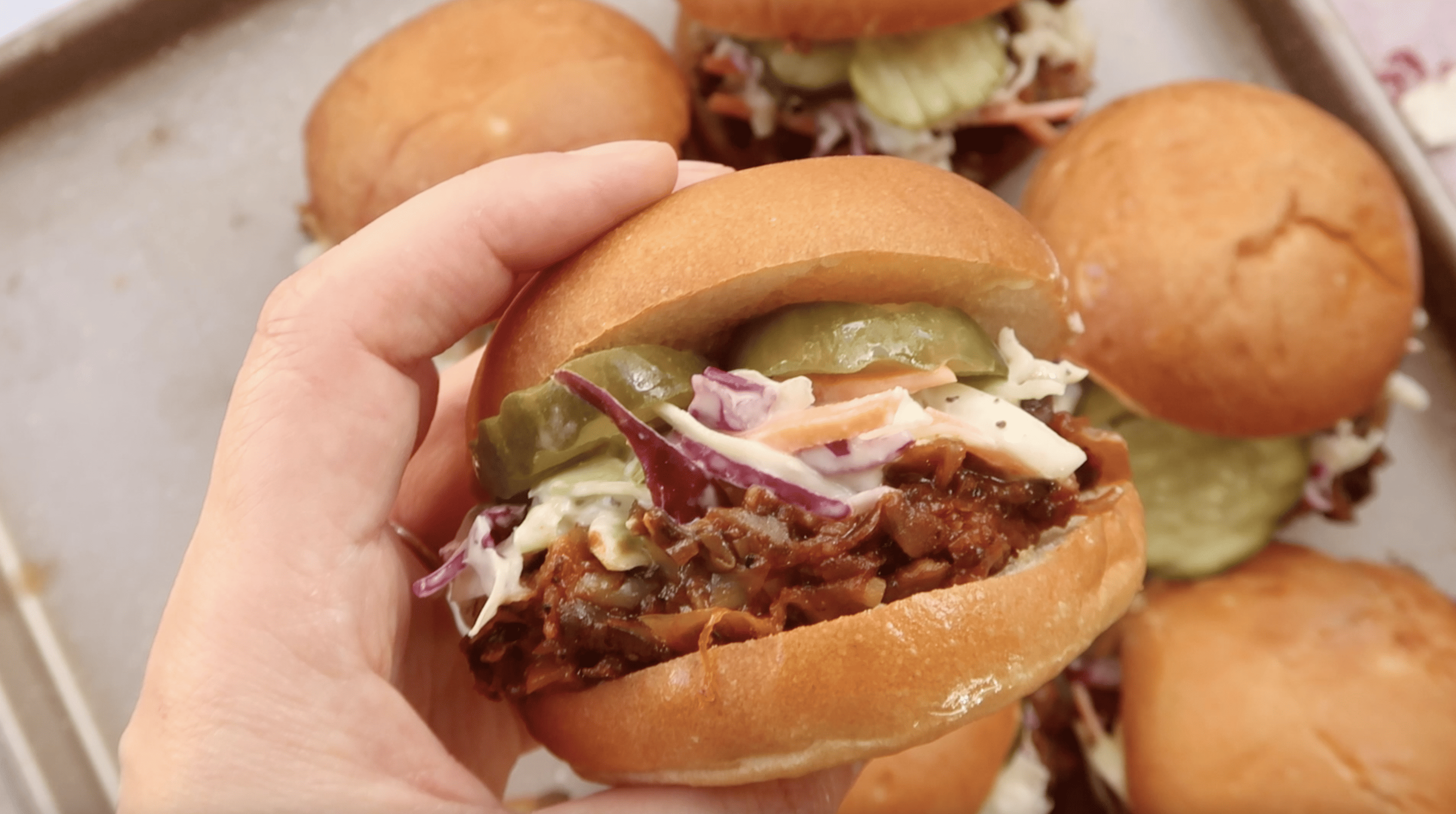 a hand holding a vegan pulled pork slider sandwich