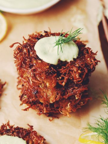 a stack of crispy vegan latkes with a dollop of vegan sour cream on top with a dill frond garnish