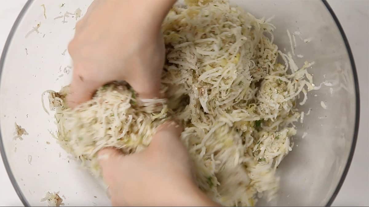 hands mixing latke mixture together in a bowl