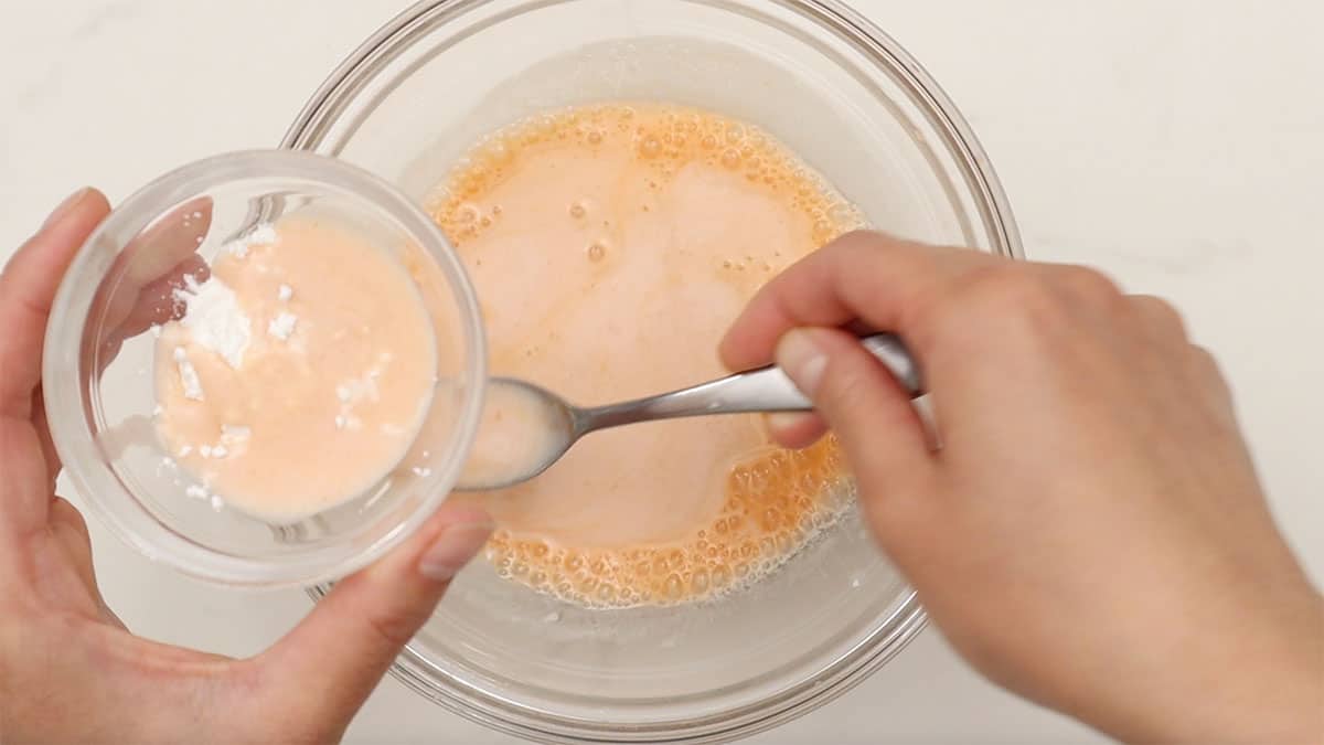 a mixing bowl with milk and hot sauce combined and cornstarch being stirred in