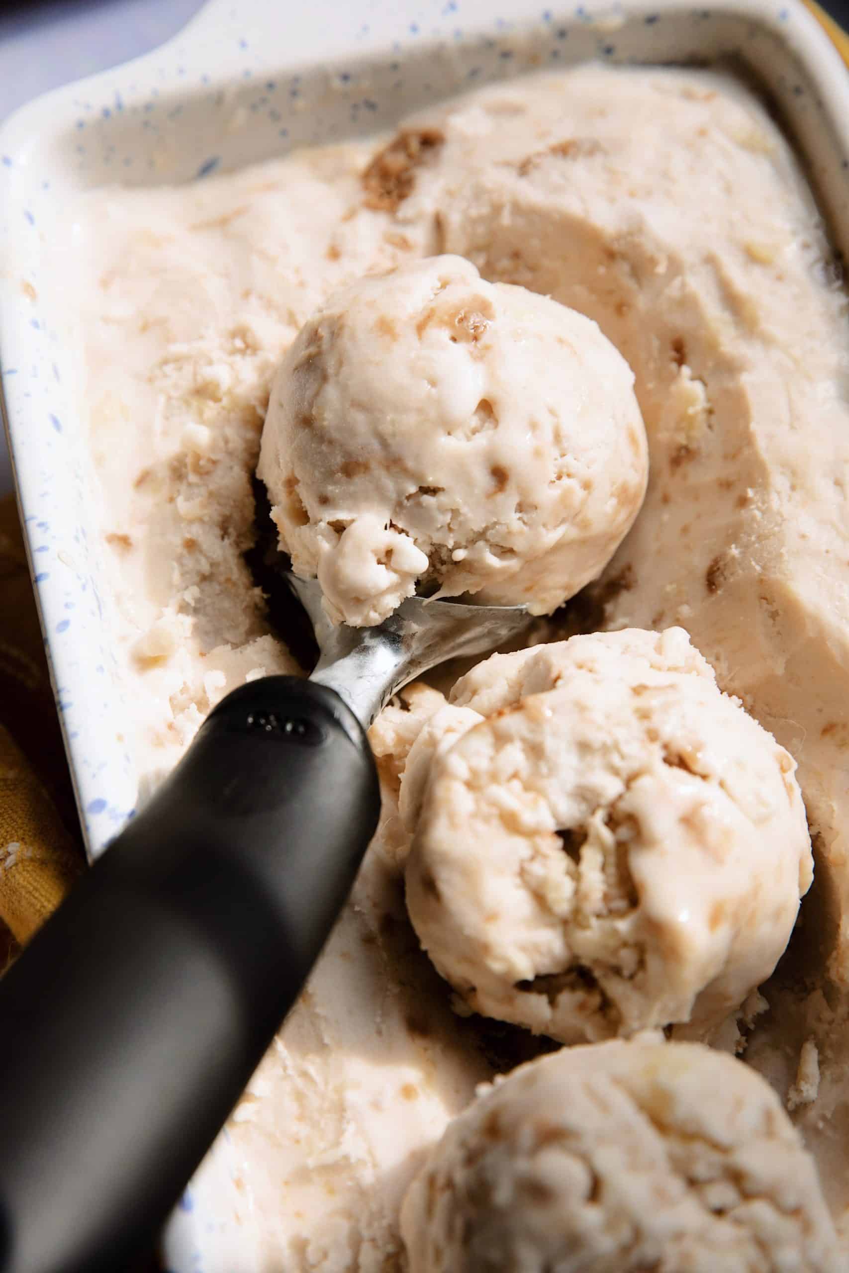 diners view of a baking dish containing vegan pineapple ginger snap ice cream with a scoop in it showing three scoops of ice cream on top of the base